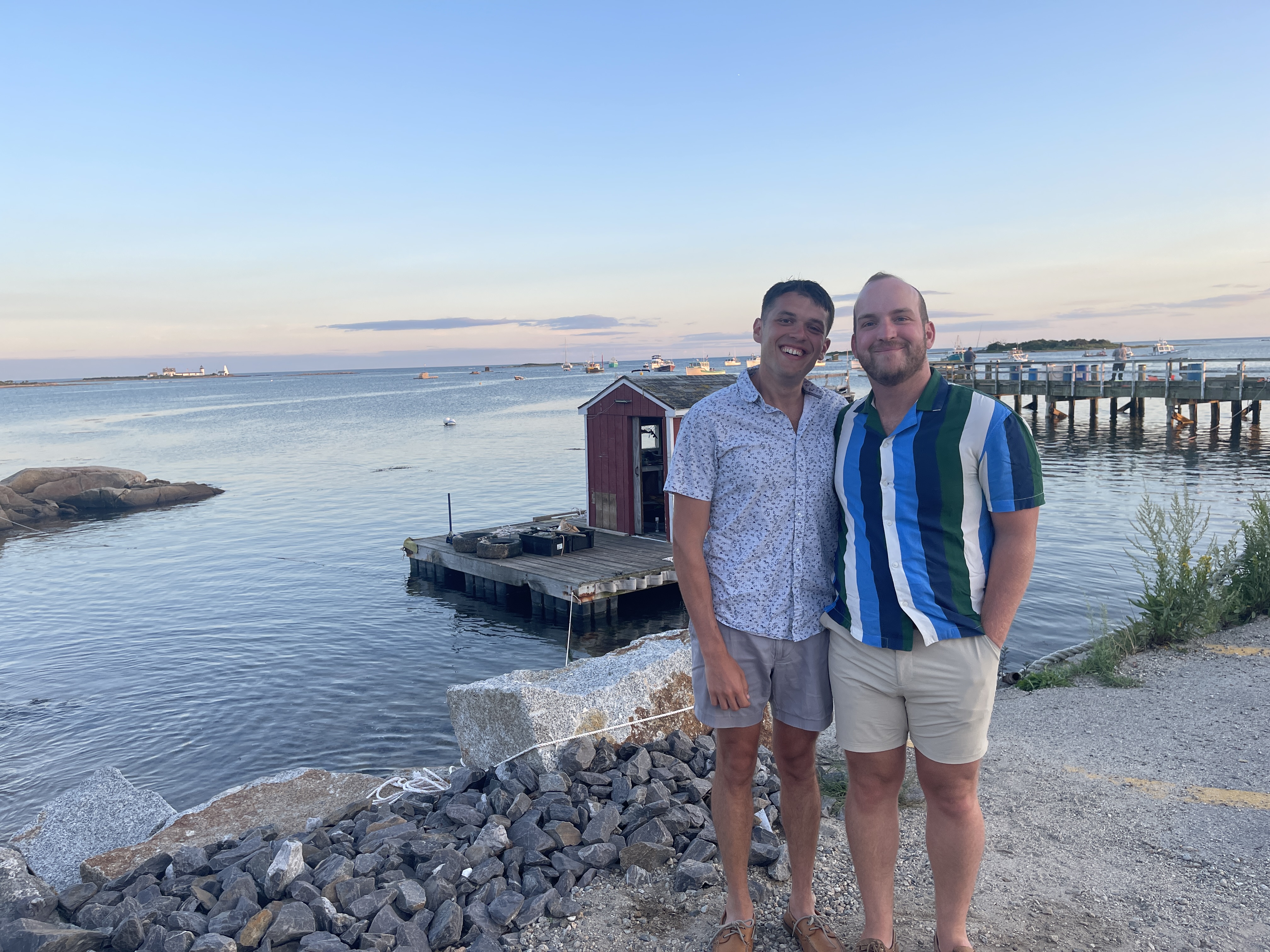Ian and Zach at golden hour by a harbor dock with boats in the background