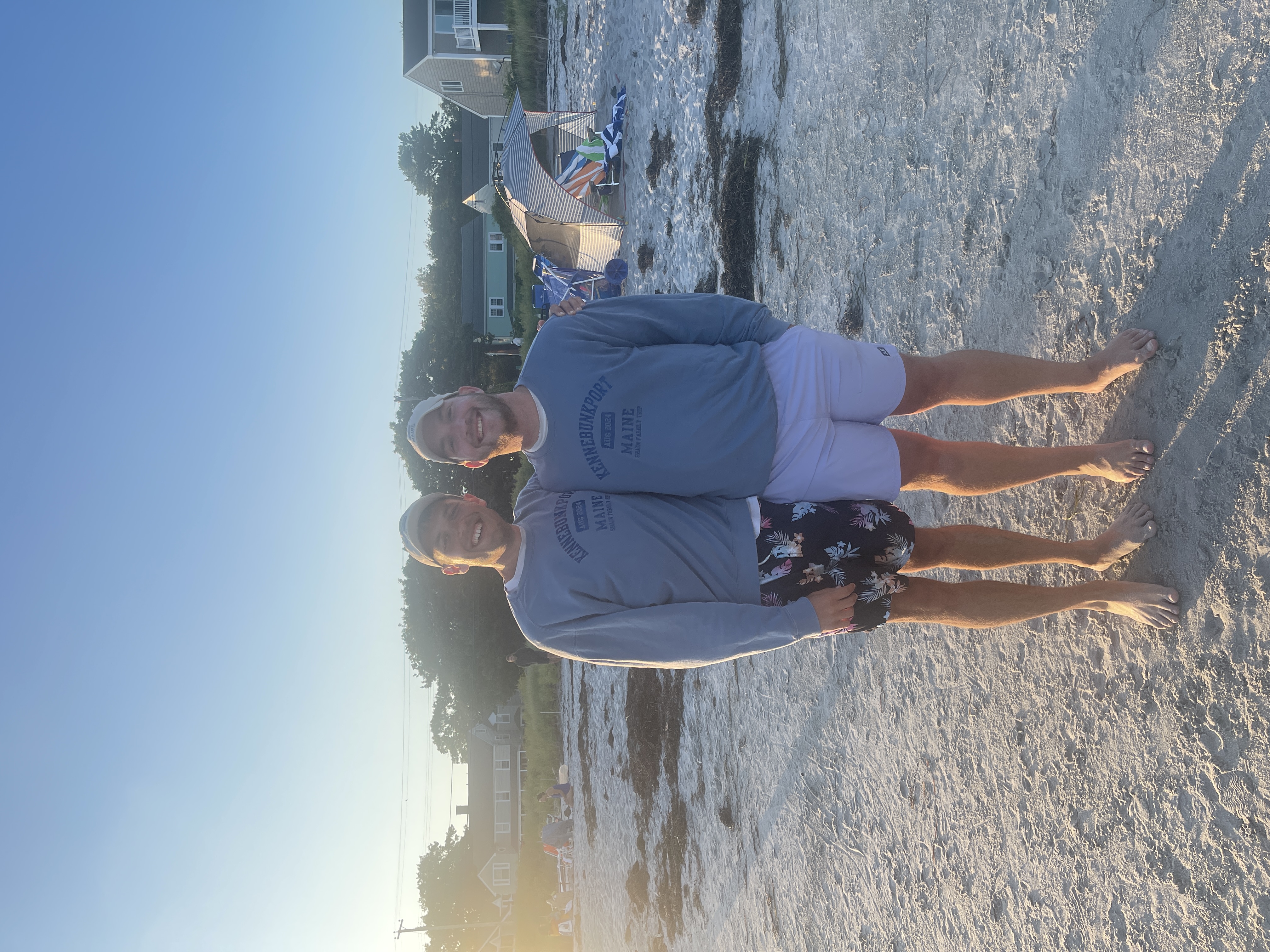 Ian and Zach in matching Kennebunkport sweatshirts on a beach at sunset