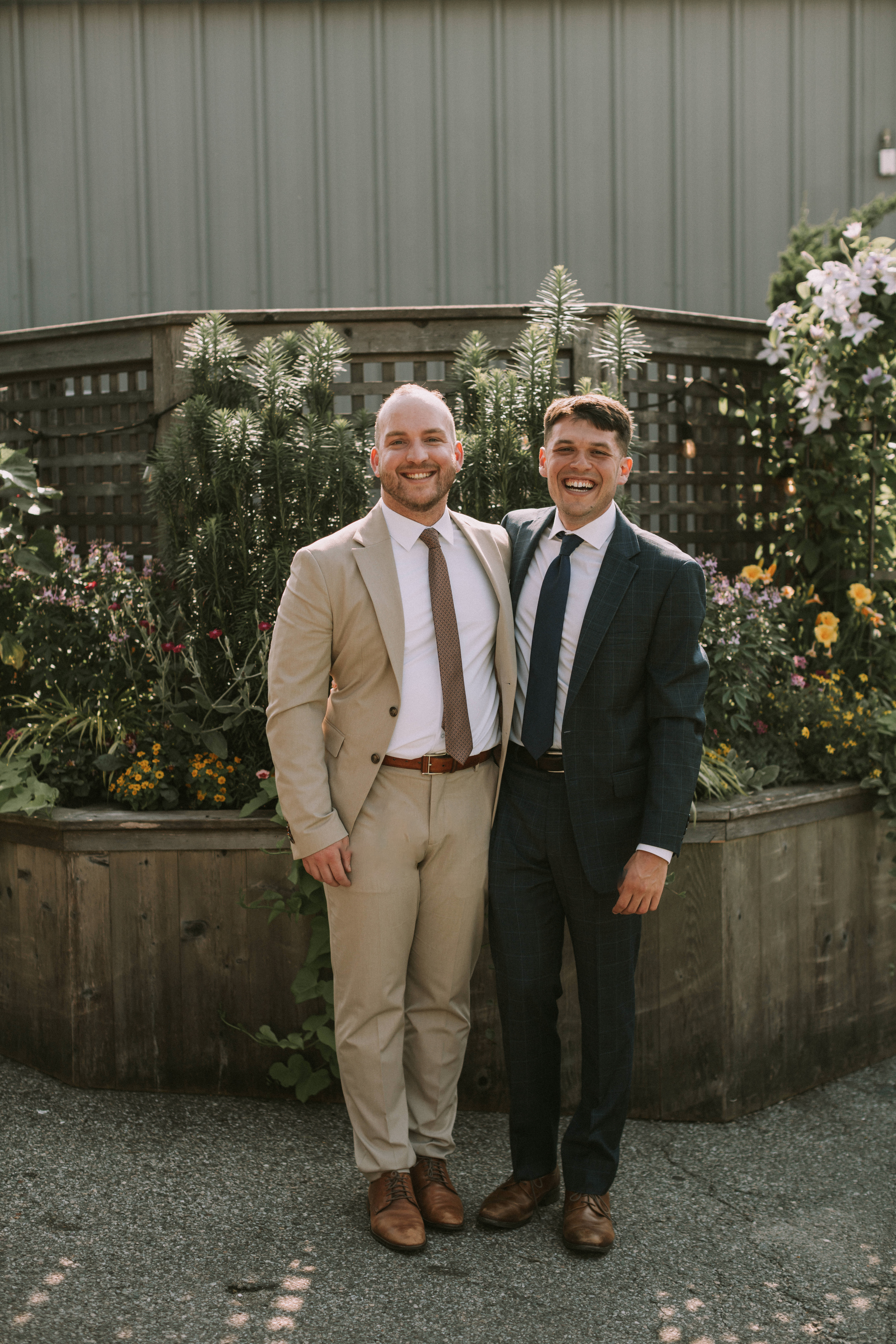 Ian and Zach dressed up and smiling in front of a garden planter full of flowers